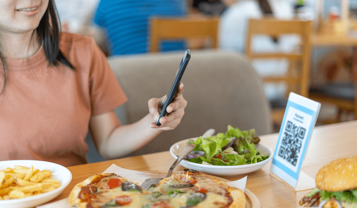 a woman sitting at a restaurant table scanning a qr code