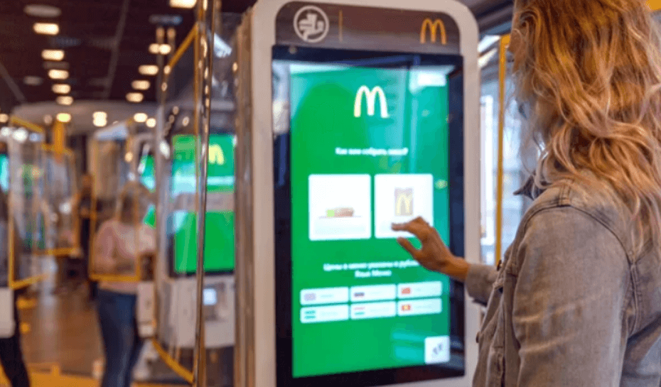 a woman standing in front of a mcdonald's digital kiosk